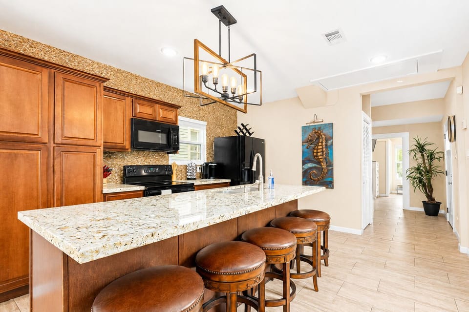 Spacious kitchen with granite breakfast bar, four leather stools, wood cabinets, black appliances and modern geometric pendant lighting.