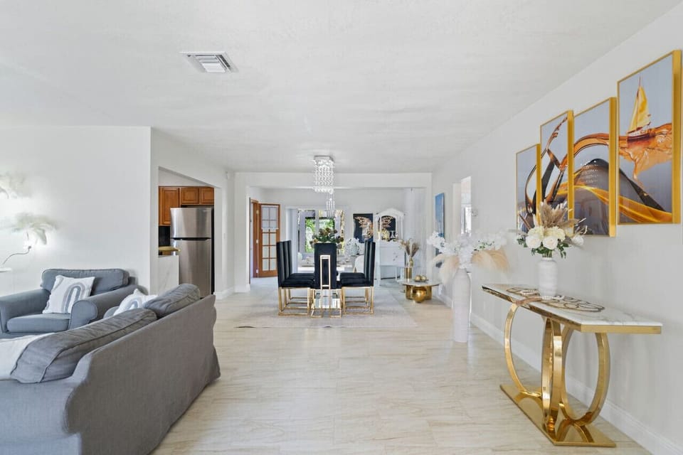 ✨ Stunning Open Concept Design! Seamless flow from living to dining with crystal chandelier, gold accents & modern artwork. Bright, spacious layout perfect for gatherings. Complete Hollywood Beach villa with game rooms, hot tub & beach 3min away!
