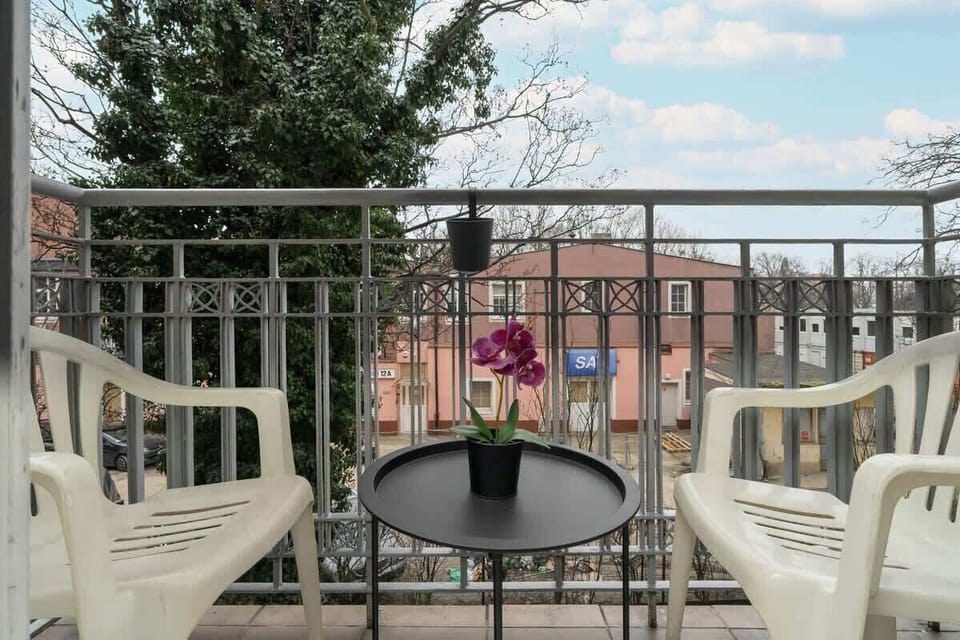 A charming balcony with a wrought iron railing, a small table, and chairs, offering a pleasant outdoor retreat with city views.

