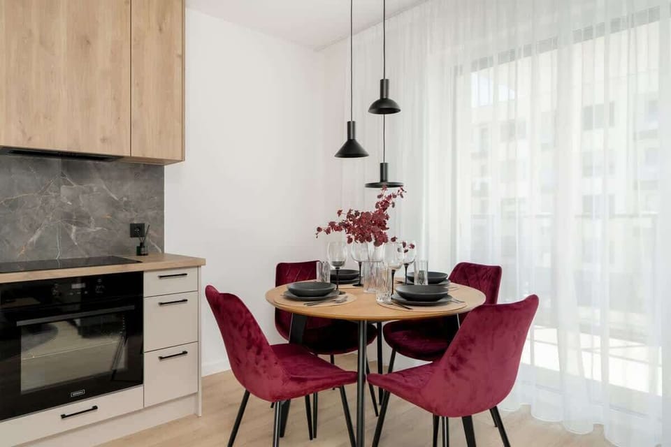 A wider angle of the dining area and kitchen, showing the light wood cabinets and red decor elements.