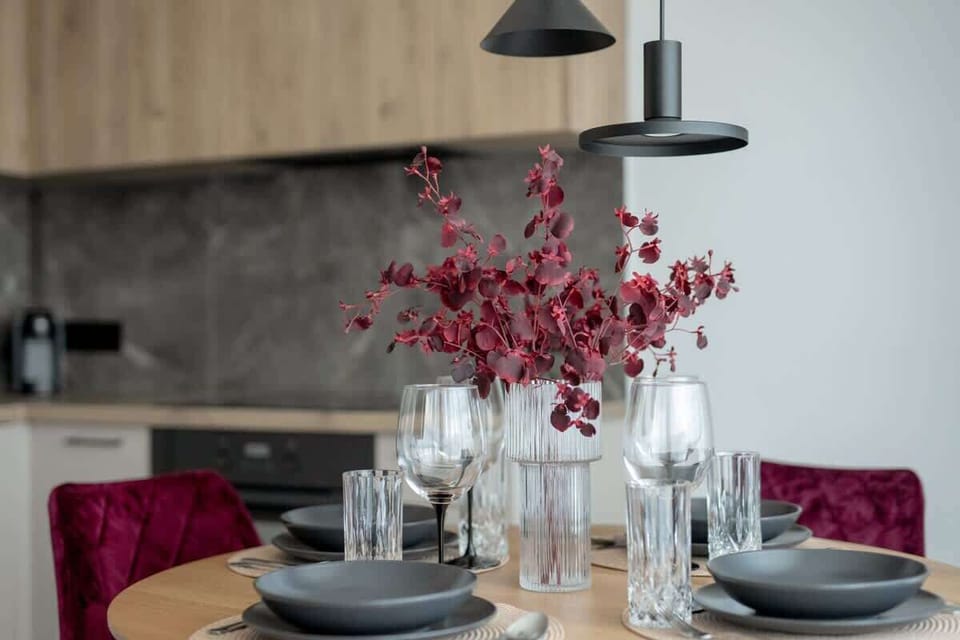 Another view of the dining table, set with black plates, wine glasses, and red flowers in a vase.