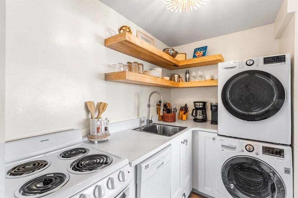 A compact kitchen featuring a stove, sink, dishwasher, and a stacked washer/dryer unit.