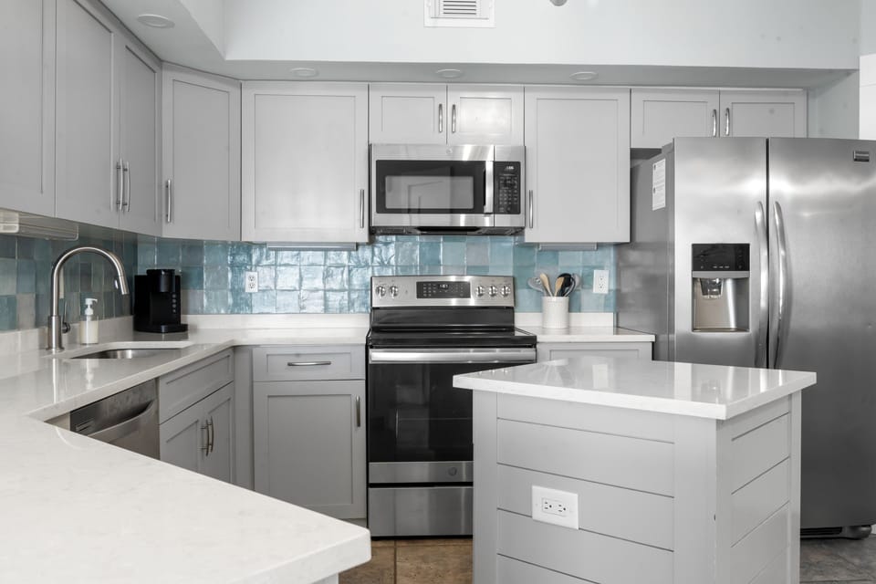 Bright modern kitchen with island, stainless appliances, and coastal tile