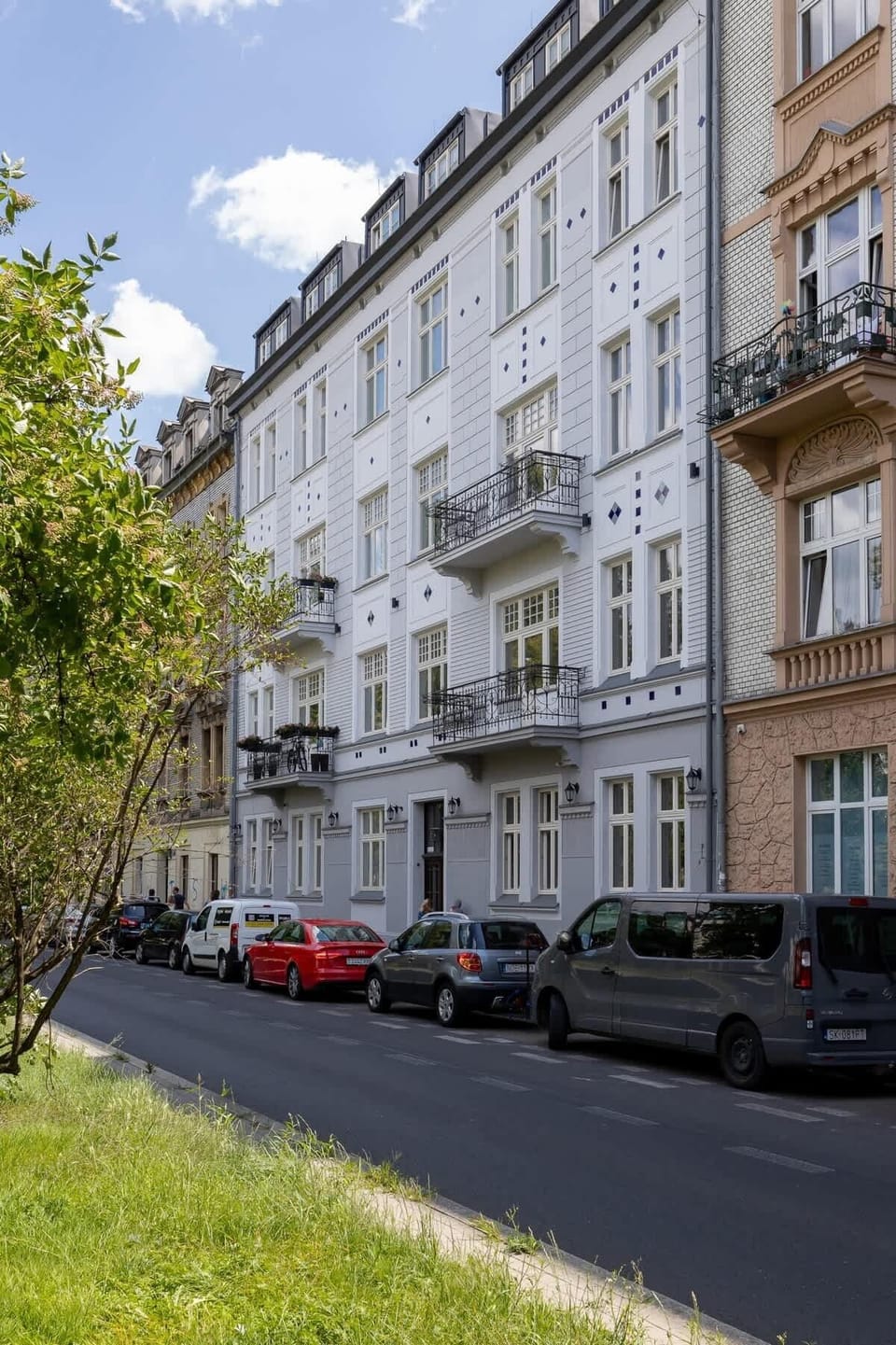 A green urban street view lined with mature trees and historic buildings.

