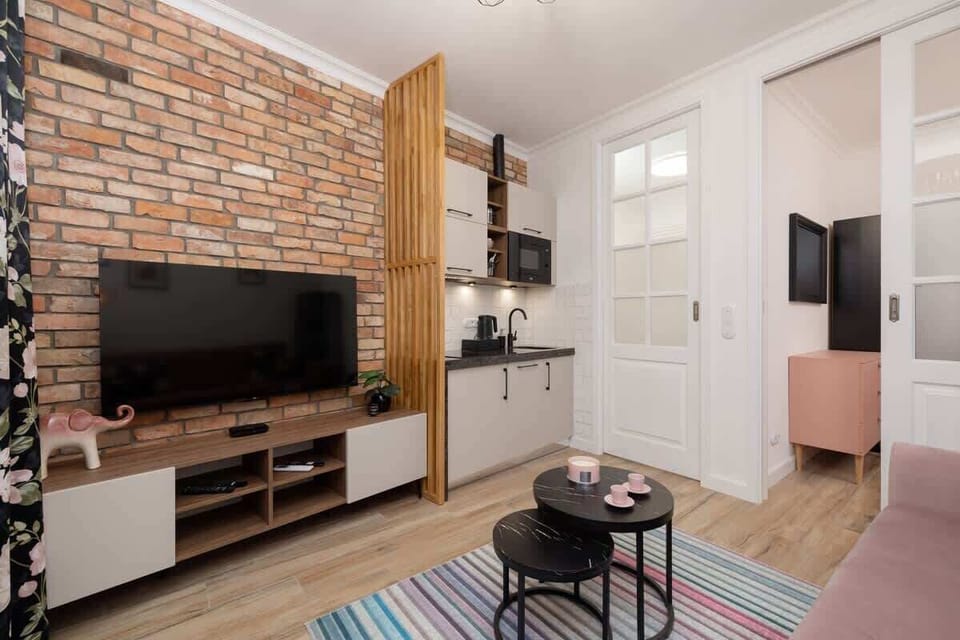 A spacious living room with an exposed brick wall, a mounted TV, and a pink sofa facing a media unit.