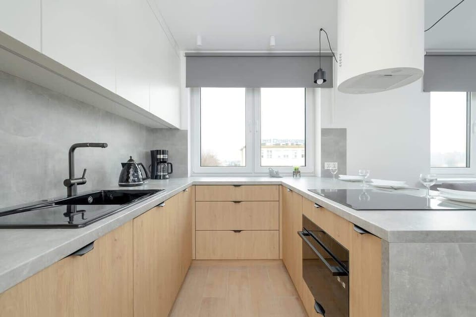 A contemporary kitchen with light wood cabinets, a gray countertop, and modern appliances, blending functionality with style.

