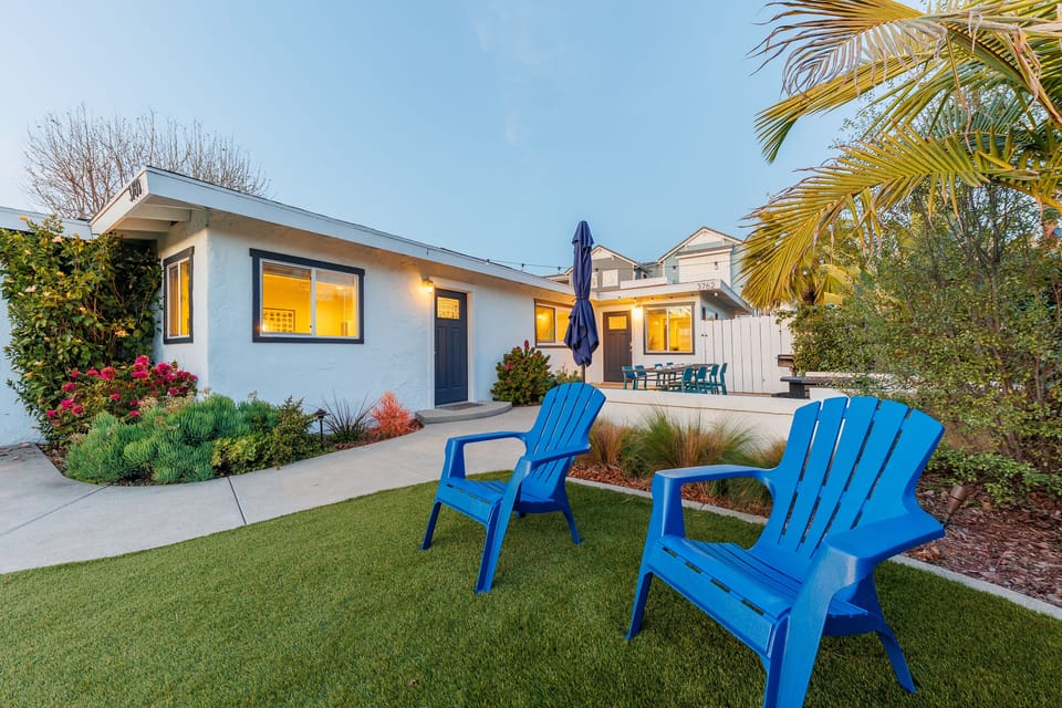Grassy backyard with blue Adirondack chairs and tropical landsca