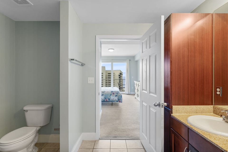 View from the bathroom into a bright bedroom with cityscape windows.