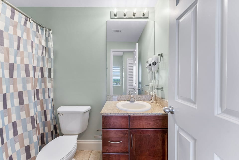 Compact bathroom with a patterned shower curtain and wooden vanity.