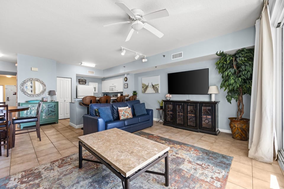Relax in your bright, welcoming living space with plush seating, ceiling fan, and large TV. Sunlight fills the open layout—perfect for unwinding after exploring nearby beaches.