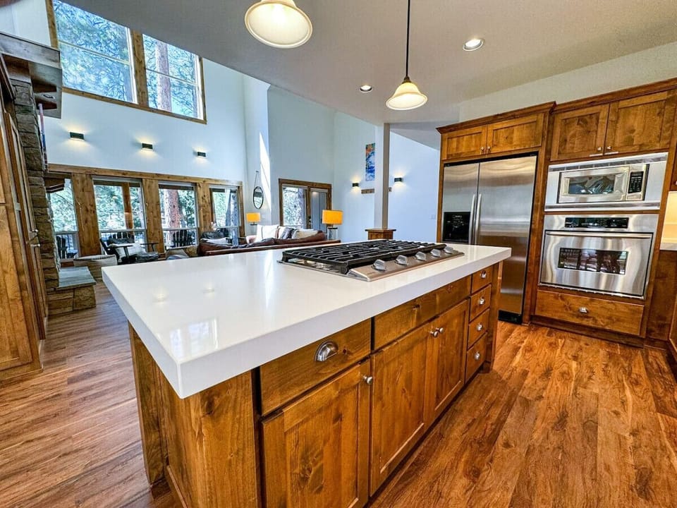 Prepare meals in this fully equipped kitchen featuring stainless steel appliances, a spacious island, and scenic views of the living area and towering pines