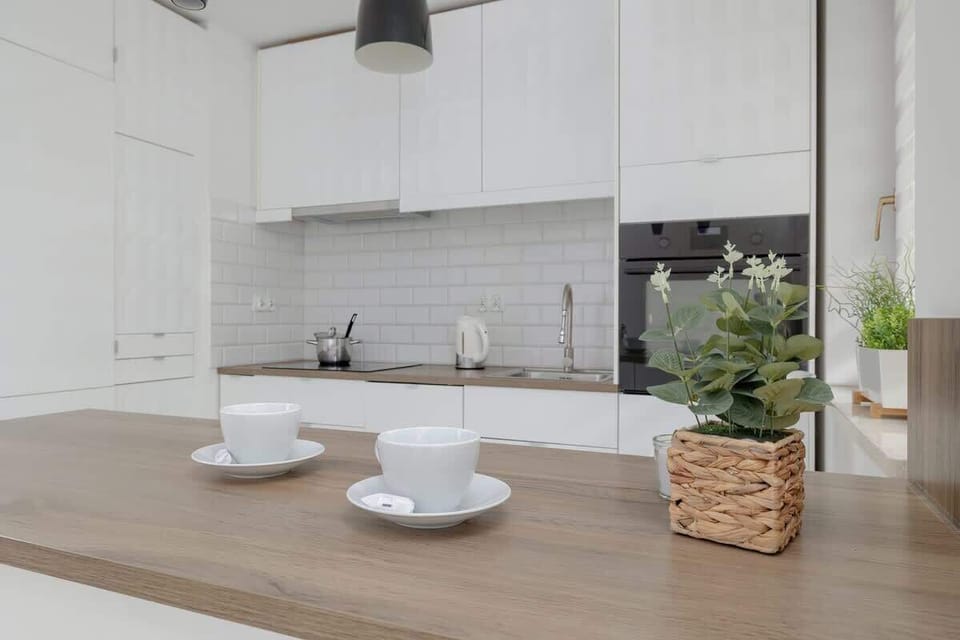 A close-up of the kitchen countertop with a natural wood finish, white cabinets, and decorative elements like a potted plant.







