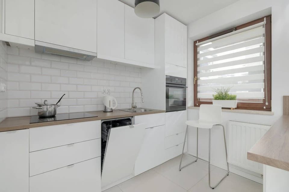 A sleek white kitchen featuring contemporary cabinets, a tiled backsplash, and a black faucet for a clean, minimalist look.

