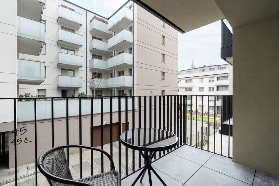 A small outdoor balcony with a round table and two chairs, providing a cozy space to enjoy the outdoors. The balcony overlooks the apartment complex.