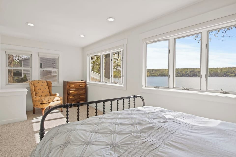 Bedroom with metal bed frame and windows overlooking the lake