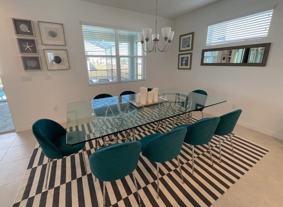Elegant dining room with a glass table and teal chairs, perfect for gatherings in a bright, art-filled space.