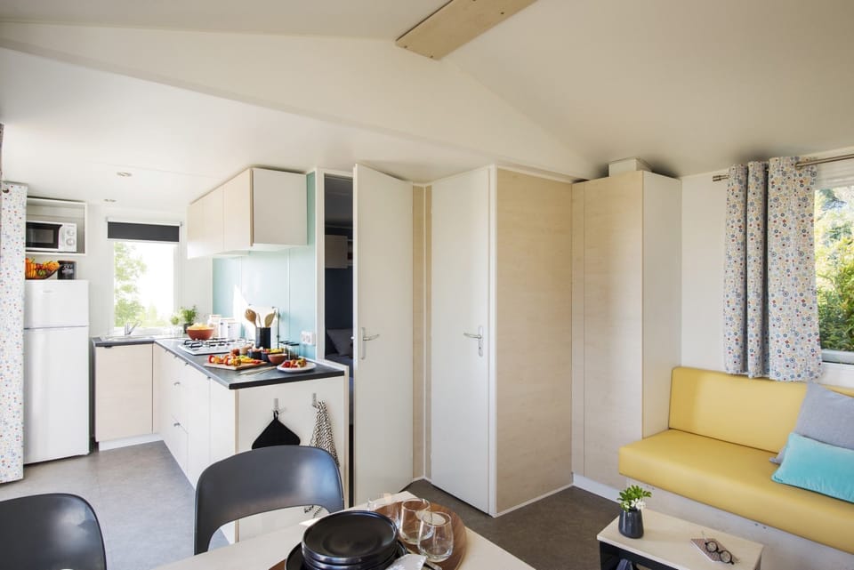 The cozy living area of this 2BR mobile home features a bright kitchenette and inviting seating, perfect for family meals after a day at the beach.