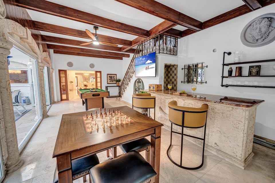 The covered patio, featuring a bar area with a pool table, boasts floor-to-ceiling windows providing seamless access to the heated pool.
