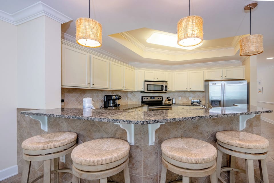 This modern kitchen features stainless appliances, granite countertops, elegant lighting, and a breakfast bar with seating