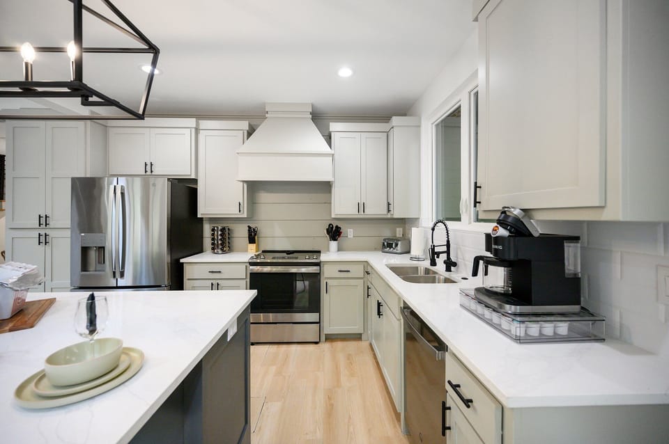 Modern kitchen w/ white cabinets, stainless steel appliances, & coffee maker.