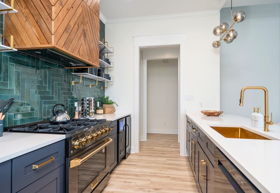 A Modern Kitchen With Sleek Cabinets, Gold Fixtures And A Long Island With White Countertops Extending Into A Casual Dining Area, All Under Warm, Inviting Lighting.