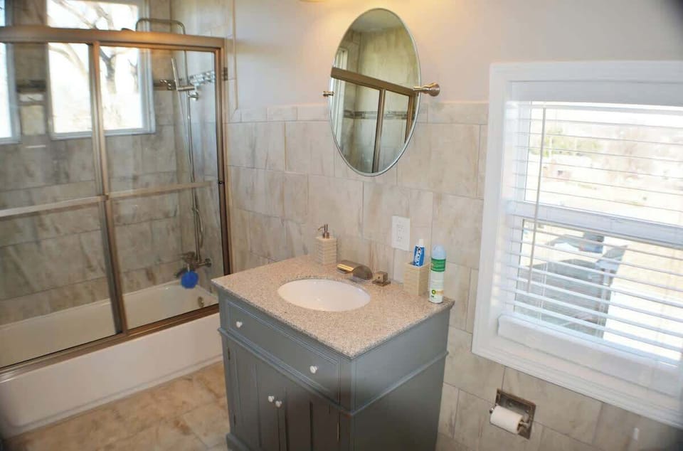 Step into refinement in this well-appointed bathroom. A sleek sink complements a stylish shower, both bathed in natural light from a window adorned with tasteful blinds. 