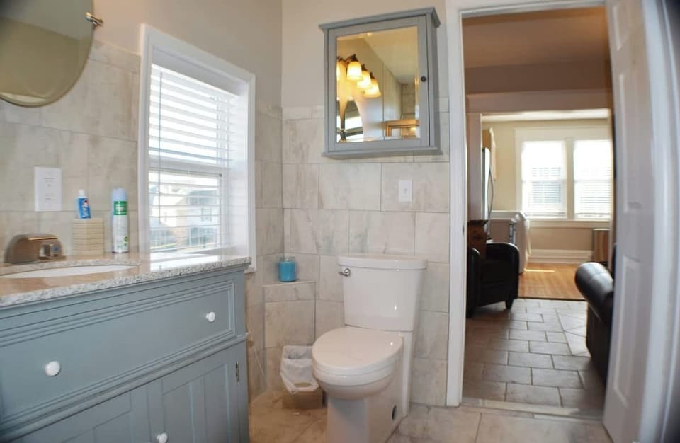 A serene bathroom scene unfolds with a pristine white toilet beside a stylish sink. The ambiance is complemented by a soothing bath and a mirror on the wall, creating a tranquil retreat where cleanliness meets elegance.
