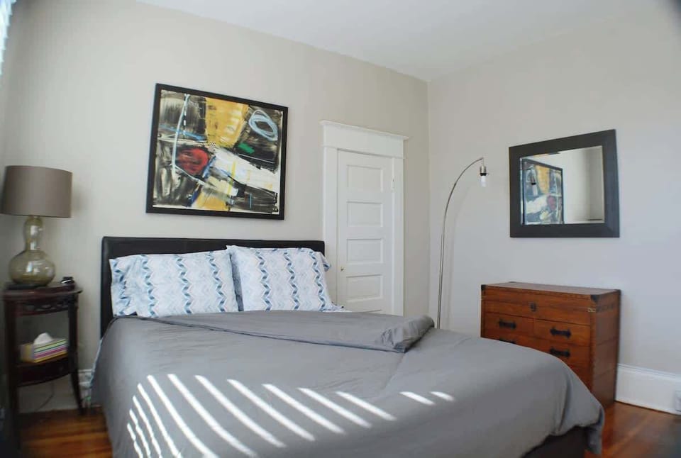 Discover serenity in this bedroom retreat. A welcoming bed rests beside artful pictures on the wall. A dresser adorned with a lamp adds warmth and ambiance, creating a haven where style meets comfort in a seamless blend.