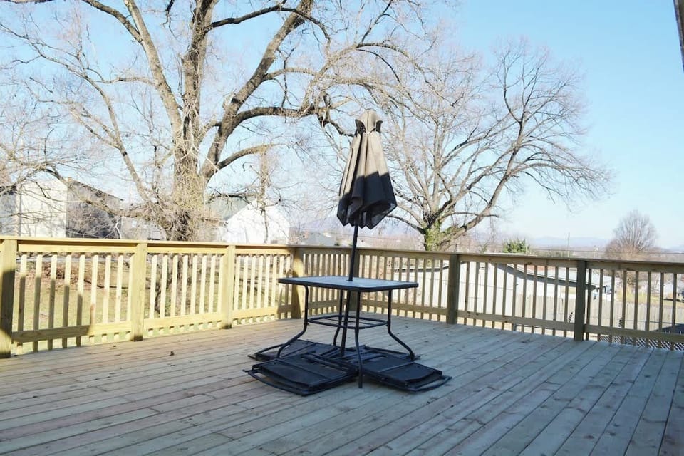 Nestled on this enchanting deck, a stylish table beckons beneath elegant umbrellas. A backdrop of a flourishing tree adds a touch of natural grace, creating an idyllic setting where relaxation and outdoor charm seamlessly converge.