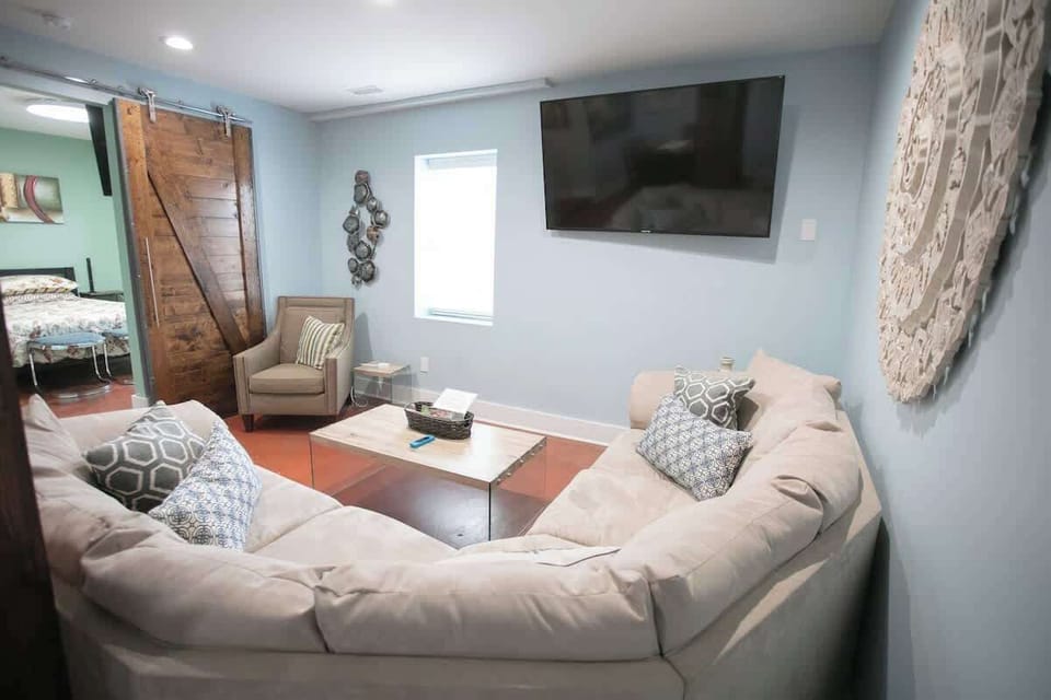 The room features a plush sectional sofa adorned with patterned pillows, centered around a wooden coffee table. A rustic barn door, wall art, and a mounted TV complete the tranquil, stylish living space.