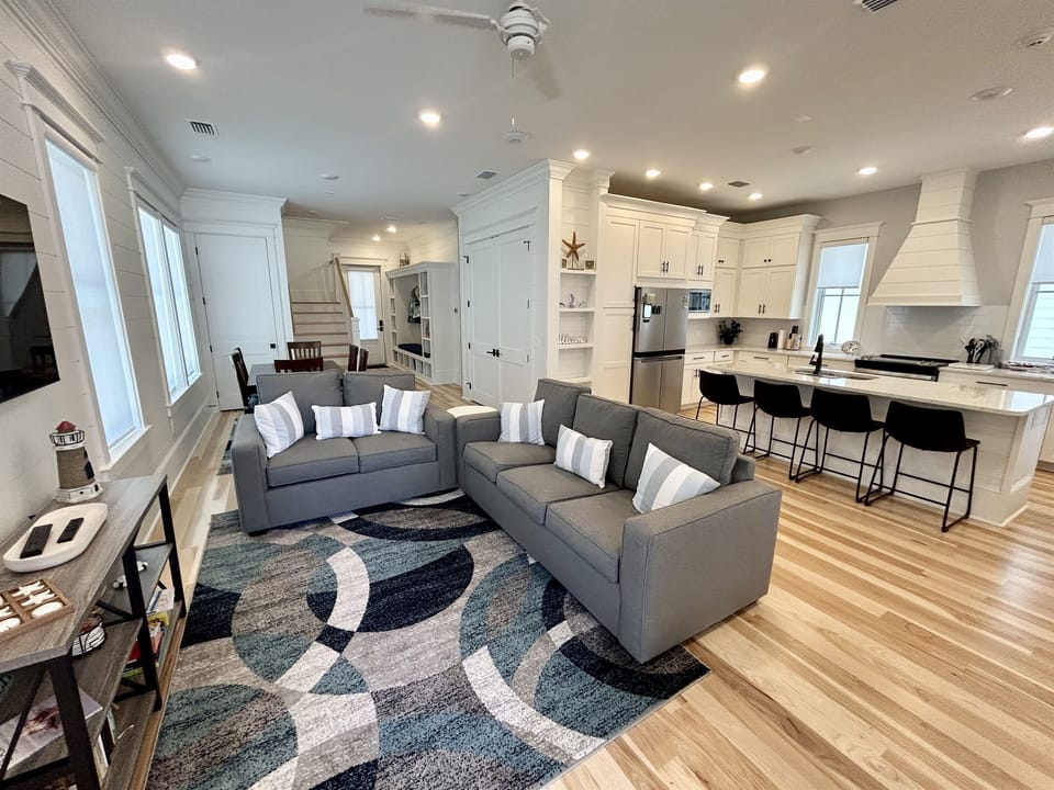 Relax in your bright, open living space where modern comfort meets coastal charm, with plush seating flowing into a chef's kitchen.
