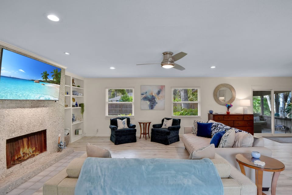 Living Room – Bright, Beachy, and Built for Lounging - Framed by windows and splashes of coastal color, this inviting space blends comfy seating, streaming-ready TV, and breezy relaxation all in one shot.