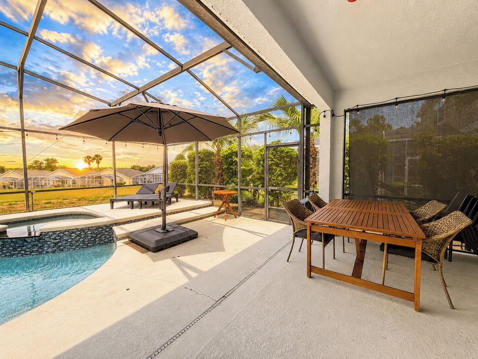 Pool area with sunset view showing outdoor dining table seating for 4 and an umbrella.