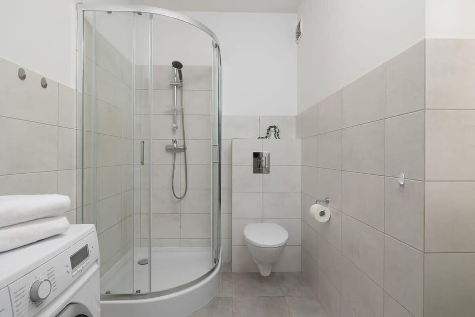 A compact but elegant bathroom with a glass shower enclosure, white tiles, and a washing machine.







