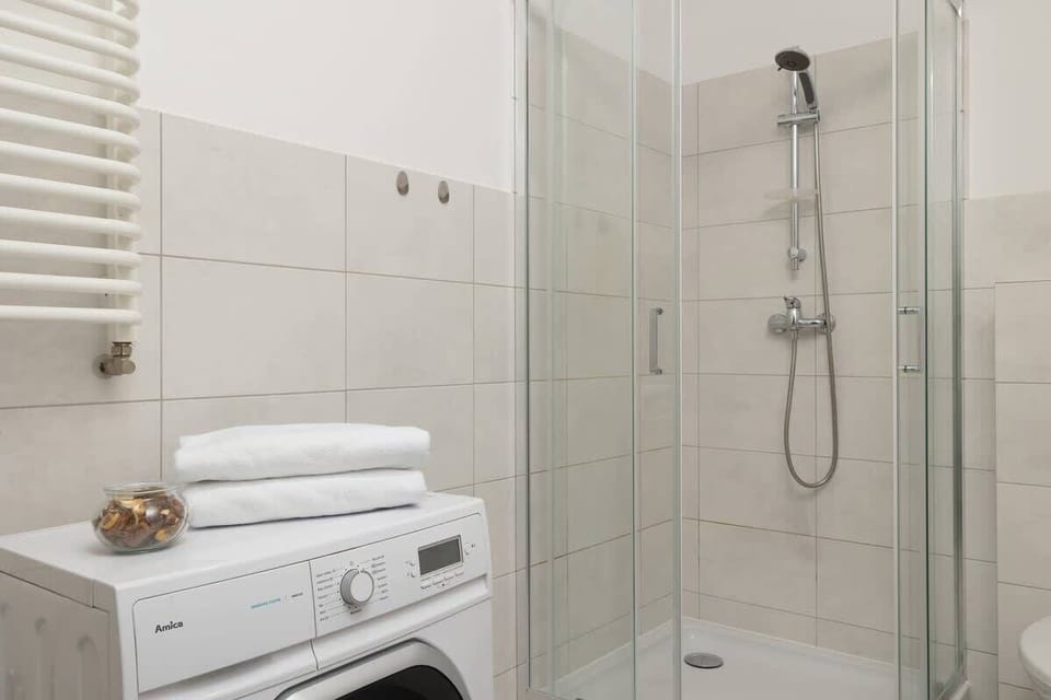 A modern bathroom with white tiles, a glass shower enclosure, and a washing machine for added convenience.


