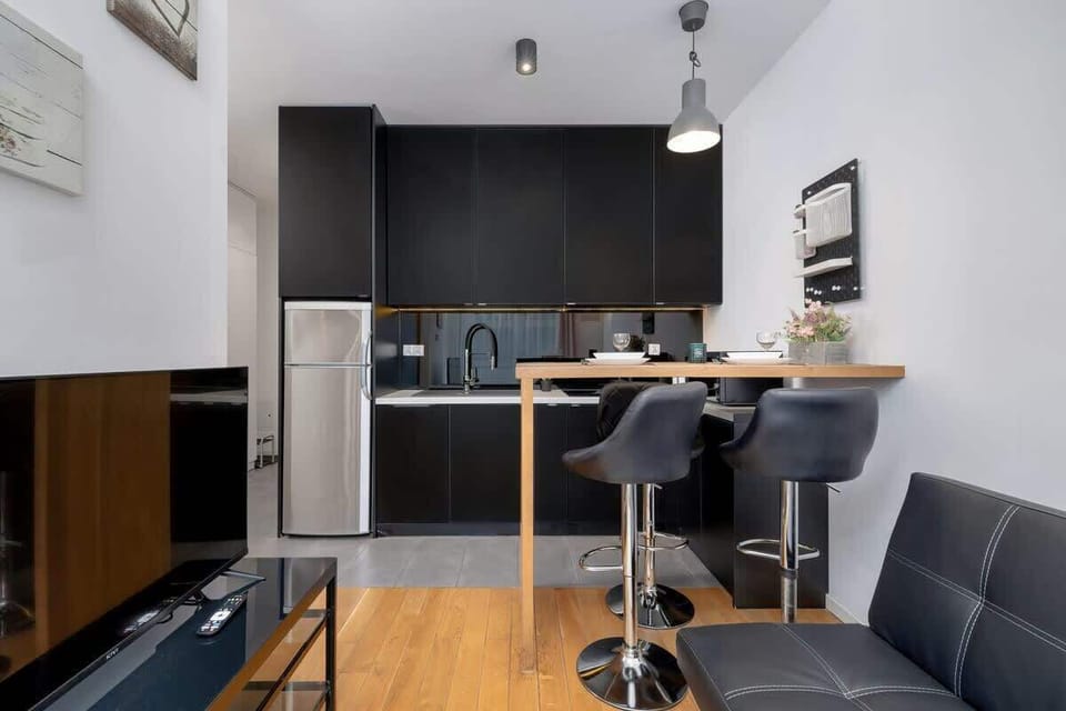 A stylish kitchen with a black and wood color scheme, a small dining table, and industrial-style lighting.

