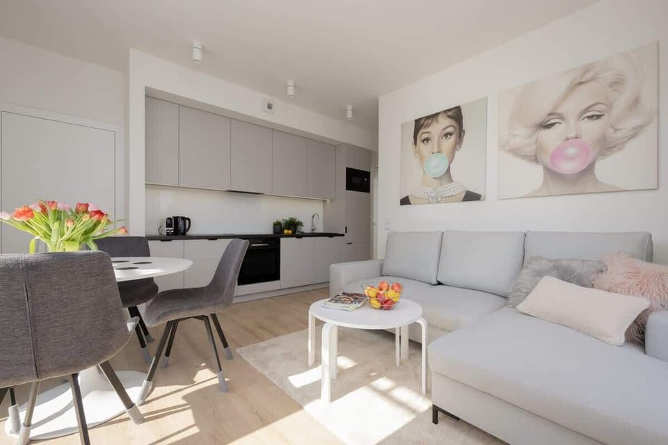 A bright lounge with modern grey seating, a coffee table, and a vase of fresh flowers.

