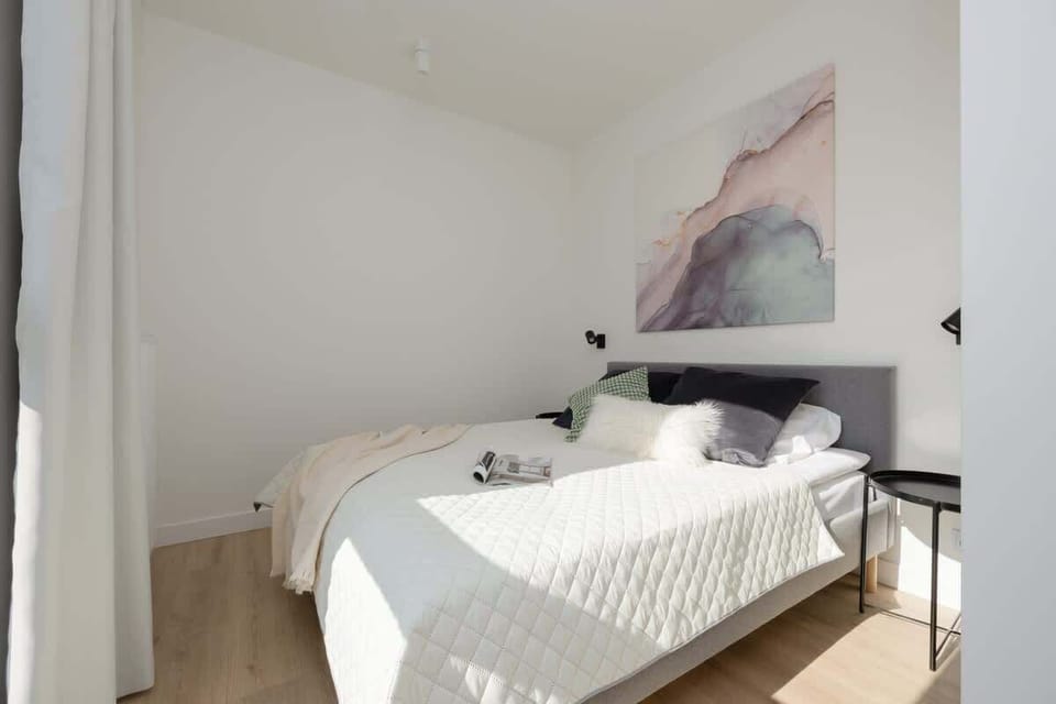 A white-toned bedroom with a patterned bedspread and minimalist furnishings.

