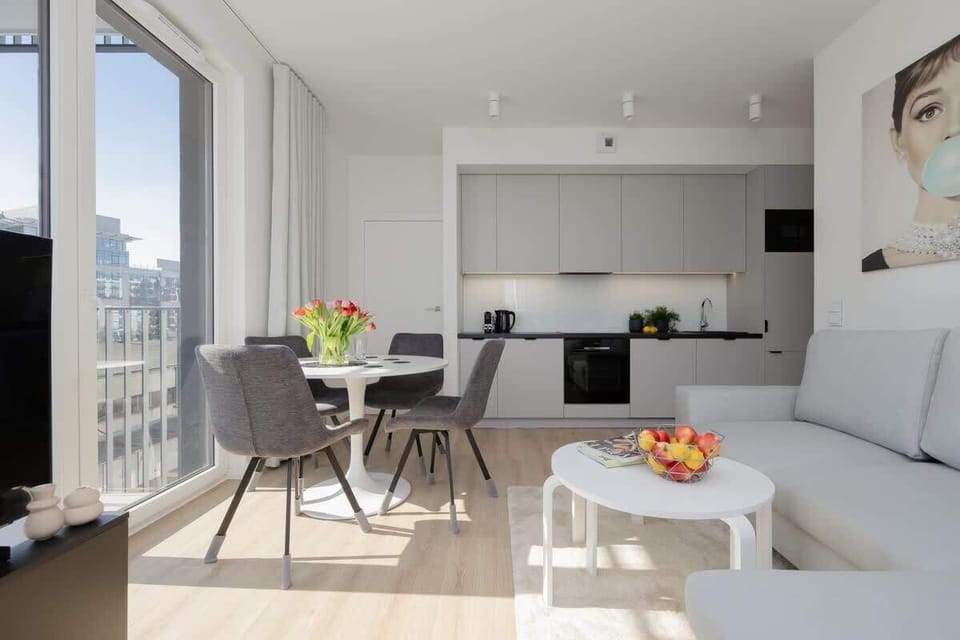 An open-plan living space with a sofa, small round table, and a kitchen area in the background.

