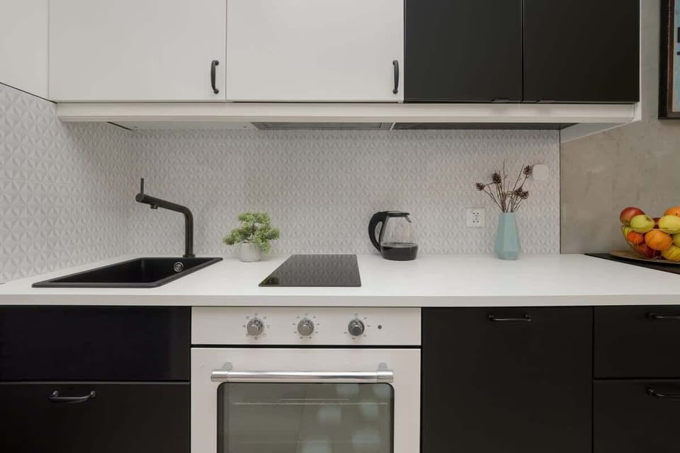 A minimalist kitchen with a white countertop, a black faucet, and decorative touches like a small potted plant.

