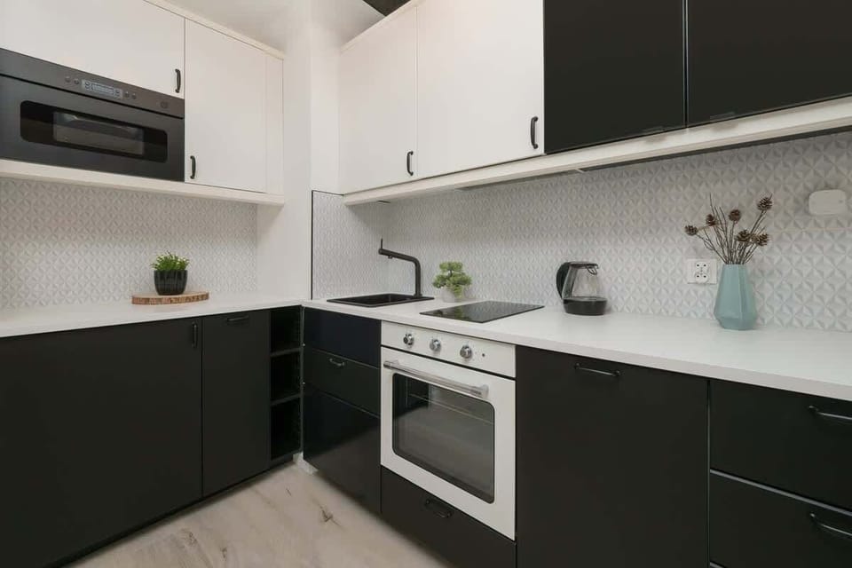 A modern kitchen with black and white cabinetry, a built-in oven, and a sleek white backsplash.

