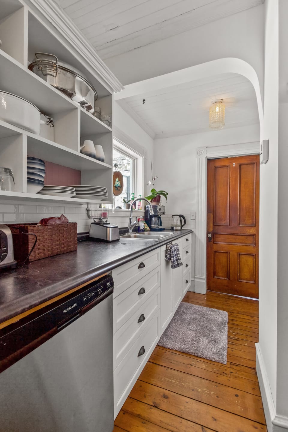 Bright kitchen with open shelving, white cabinets, and a dark countertop.