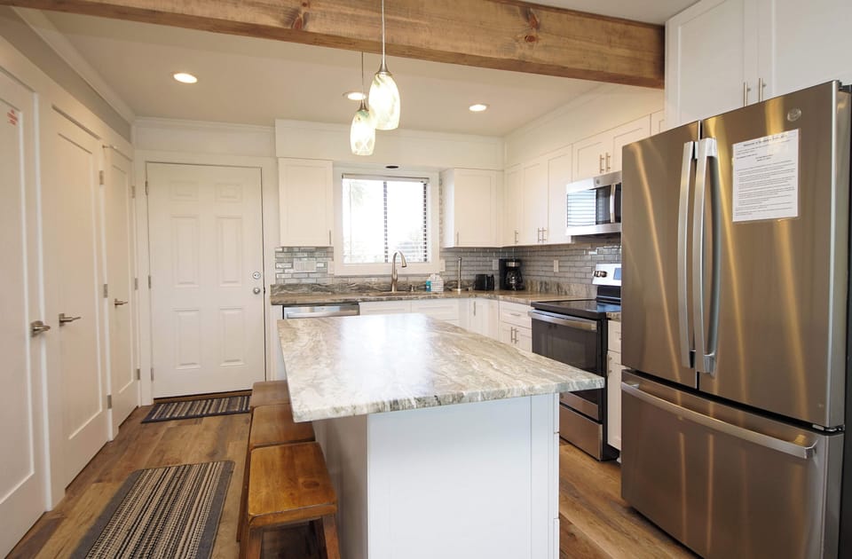 Your modern kitchen invites culinary creativity with granite counters, stainless appliances, and warm wood beams overhead.