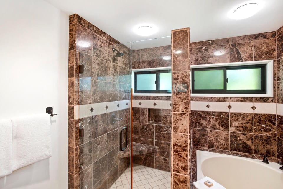 Spacious marble-tiled shower with glass enclosure and built-in bench.