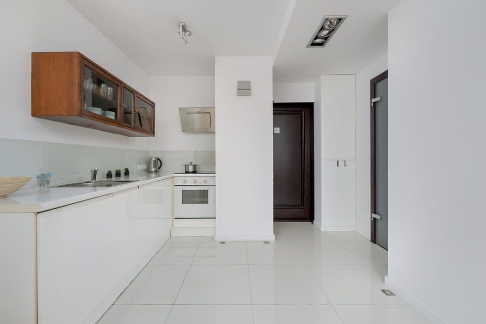 A spacious and modern kitchen with sleek white cabinetry, wooden accents, and built-in appliances.

