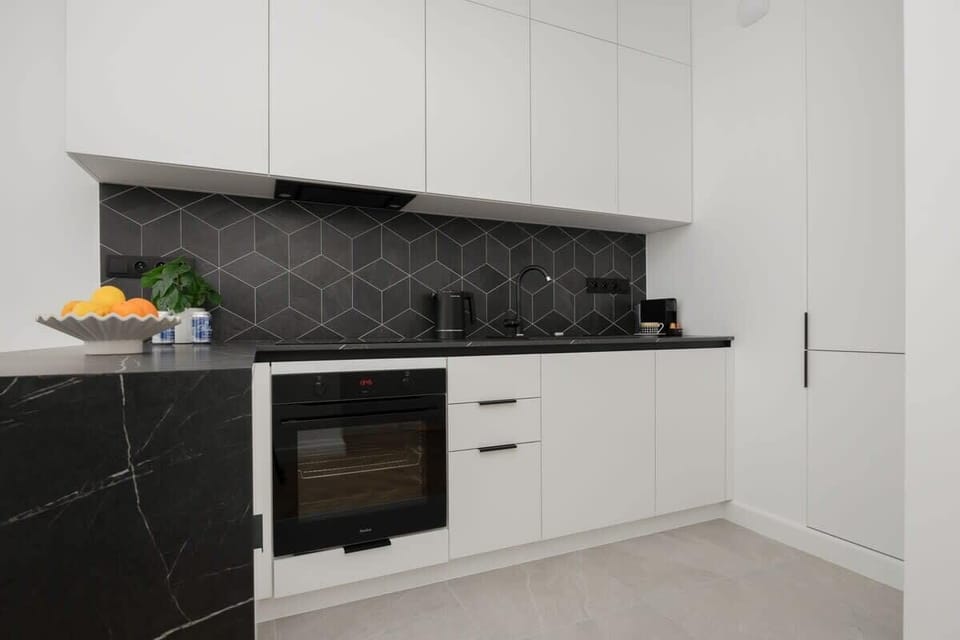 Open-plan kitchen with white cabinets, built-in oven, and dark backsplash.