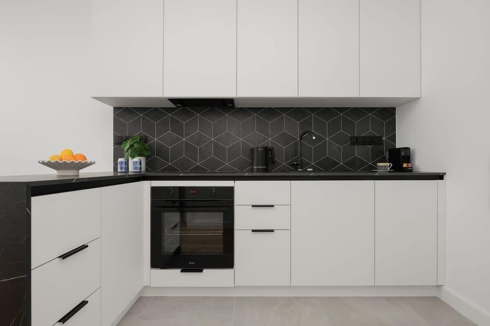 Practical kitchenette with white cabinets, built-in oven, and dark backsplash.