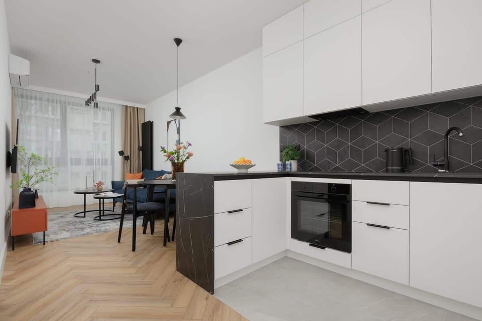Open-plan kitchen with white cabinets, built-in oven, and dark backsplash.