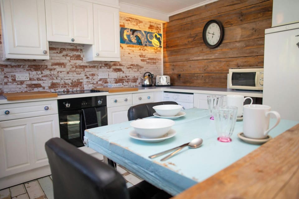 Dining table set with bowls, cutlery and mugs in a kitchen with brick backsplash
