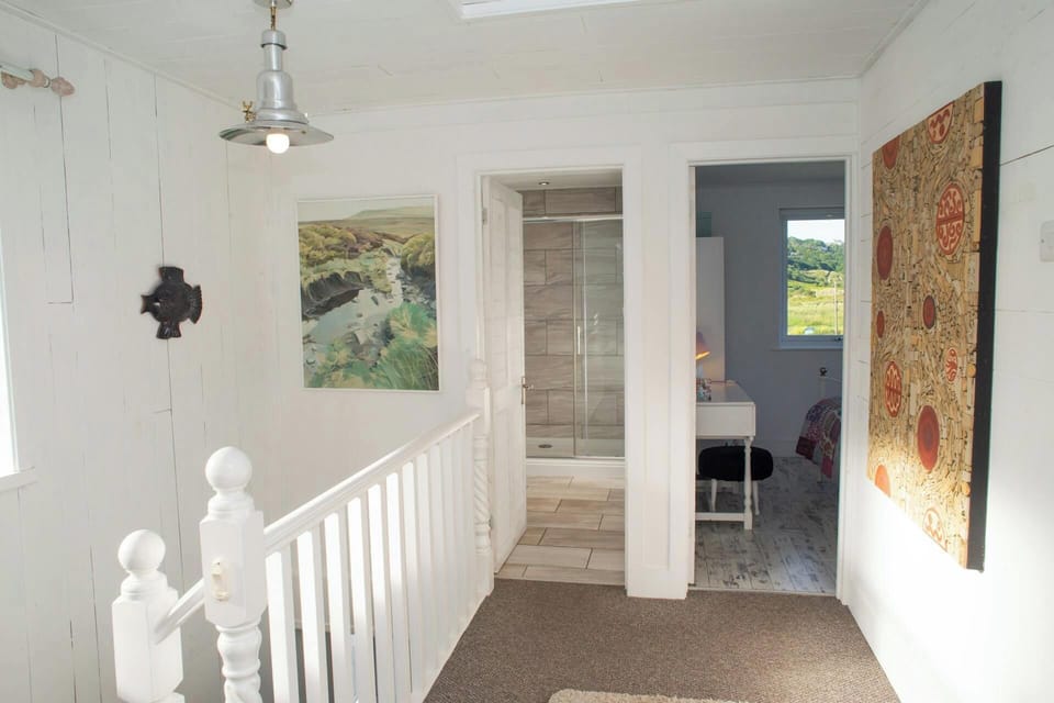 Upstairs landing with white banister, carpeted floor and open doors to bathroom and bedroom